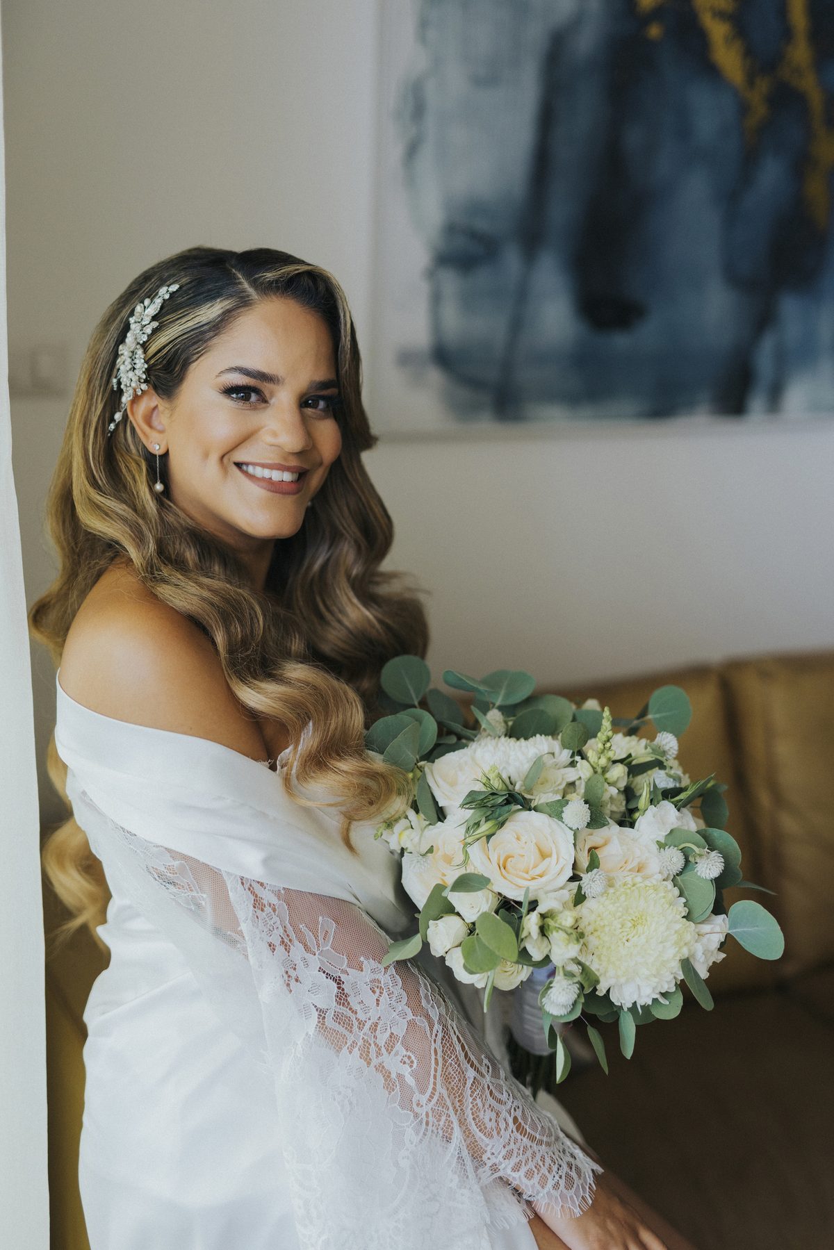 Happy bride in lace robe holding white floral bouquet on wedding morning